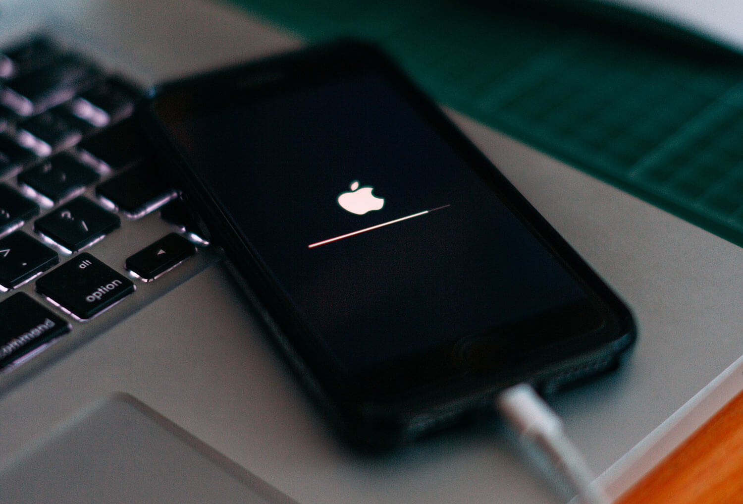 Foto de um iPhone ligado ao cabo, com a tela preta e o logo da maçã